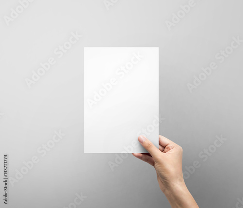 Woman hand holding blank paper sheet A5 size or letter paper on grey background.
