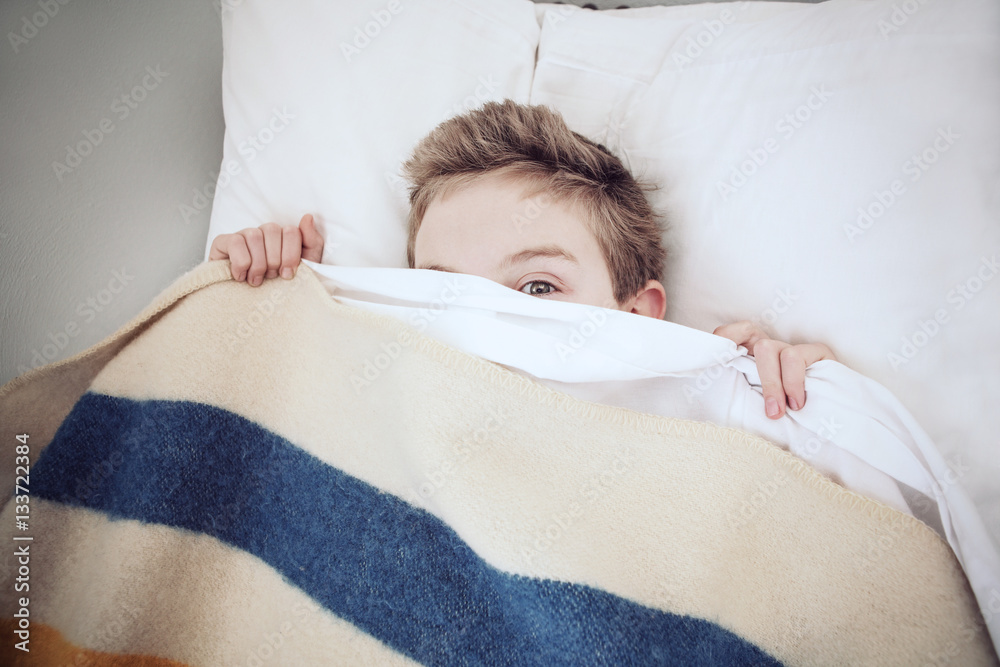 Boy hiding under the covers, peeking out Stock Photo Adobe Stock