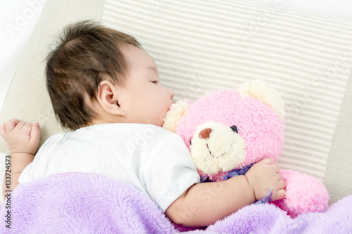 Portrait of adorable baby girl sleeping on the bed with bear dol