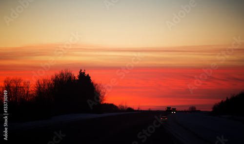 Taillights of cars on a highway under an orange sunset in a night time rural landscape © kat7213