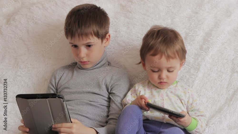 Children sitting on the couch playing on your tablet and phone to computer games