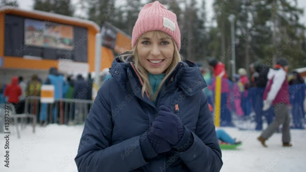 Portrait of a young smiling woman in winter clothing waiting for her friends near ski lift. Portrait of a young smiling woman in winter clothing waiting for her friends near ski lift.