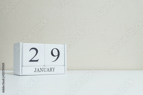 Closeup white wooden calendar with black 29 january word on blurred white wood desk and cream color wallpaper in room textured background with copy space , selective focus at the calendar