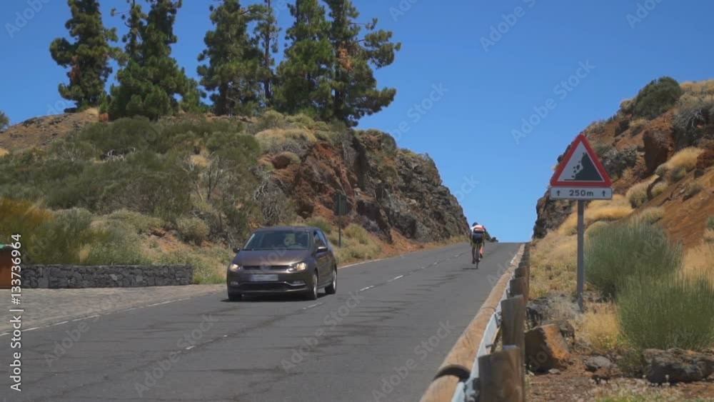 The car goes on the road to the mountain. Cyclist riding uphill