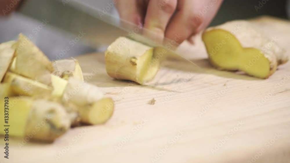 Cook cuts into cubs ginger on wooden board inside industrial kitchen Cook cuts into cubs ginger on wooden board inside industrial kitchen