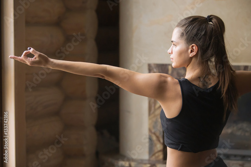 Young attractive woman practicing yoga  standing in Warrior Two exercise  Virabhadrasana 2 pose  working out  wearing sportswear  black tank top  shorts  indoor full length  home interior