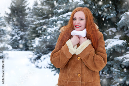 beautiful woman on winter outdoor, snowy fir trees in forest, long red hair, wearing a sheepskin coat