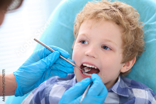 Close-up portrait of little boy opening his mouth wide during inspection of oral cavity by dentist.