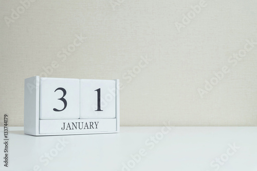 Closeup white wooden calendar with black 31 january word on blurred white wood desk and cream color wallpaper in room textured background with copy space , selective focus at the calendar