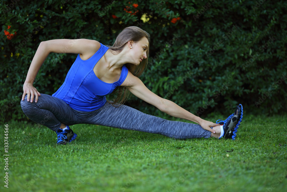 Young fitness girl trains stretching outdoors on grass