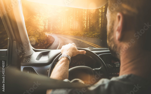 Mann fährt mit Auto durch einen Wald (Rückansicht) mit Gegenlicht photo