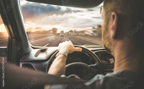 Mann fährt mit Auto über eine befahrene Autobahn (Rückansicht) mit Gegenlicht photo
