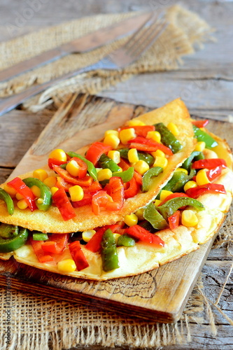 Delicious vegetable omelet on a wooden board. Fried omelet stuffed with red and green bell peppers and corn. Easy vegetarian breakfast omelet recipe. Vintage style. Closeup 
