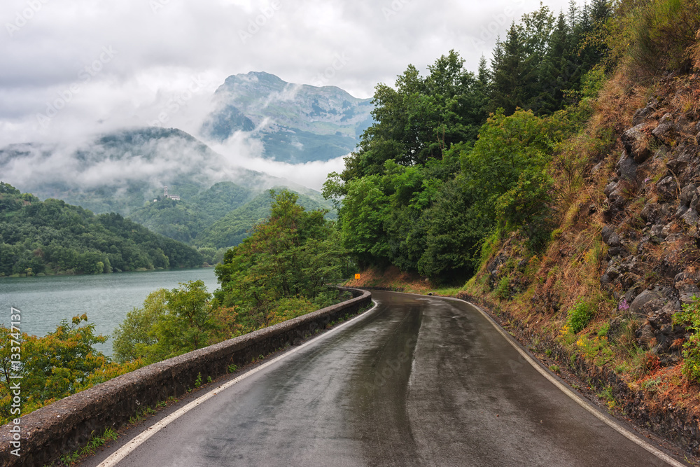 Winding road along the lake in the hills of Tuscany after the rain among the low clouds on a summer day