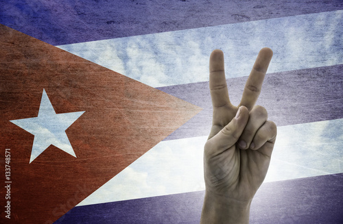 Victory symbol - two fingers against background of Cuba flag photo