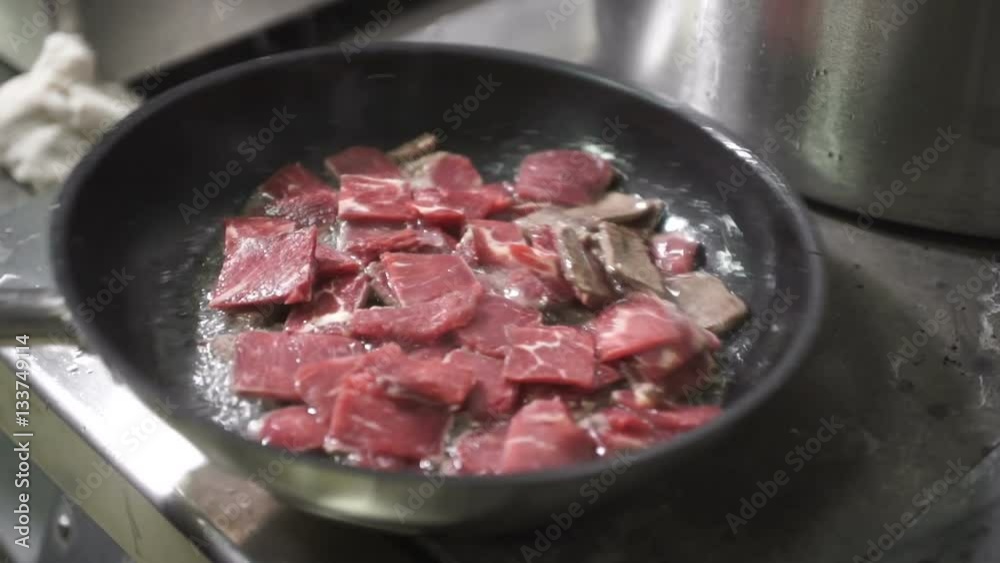 cook roasts meat in frying pan on professional kitchen in restaurant cook roasts meat in frying pan on professional kitchen in restaurant
