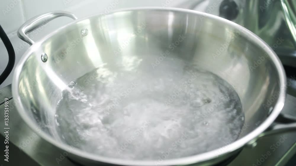 On the stove in a large metal bowl with handles water boils. On the stove in a large metal bowl with handles water boils.