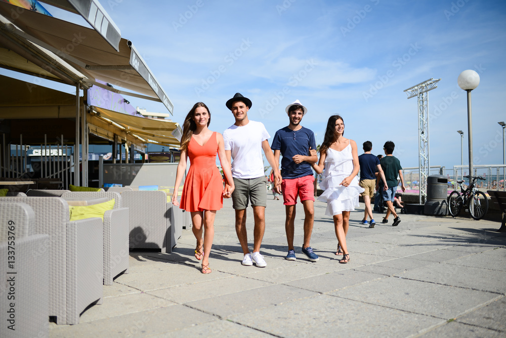 Group of young people man and woman walking on seaside of touristic resort during a sunny summer day