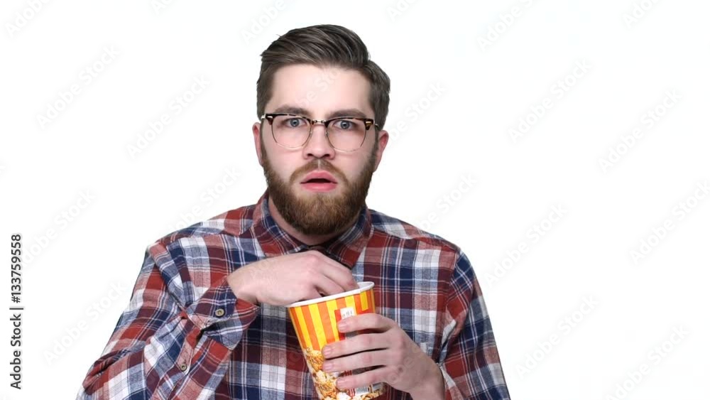 Very scared young bearded man watching horror movie and eating popcorn Very scared young bearded man watching horror movie and eating popcorn