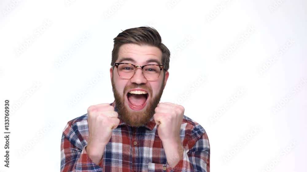 Happy young bearded man in eyeglasses gesturing and keeping mouth open while standing against white background Happy young bearded man in eyeglasses gesturing and keeping mouth open while standing against white background