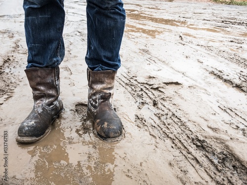 Фотография Dirty brown boots on the mud when raining