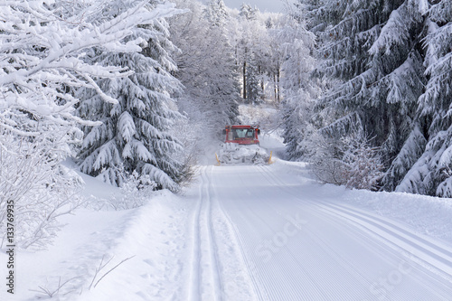 Groomed ski trail and snow groomer in sunny winter day on mountain. Trees covered with hoarfrost illuminated by the sun.
