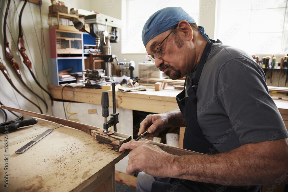 A bow maker working on a wooden bow in his workshop. A bow maker working on a wooden bow in his workshop.