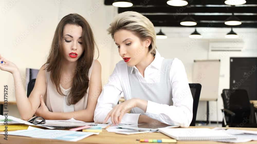Two female colleagues working together while sitting in office at the desk Two female colleagues working together while sitting in office at the desk
