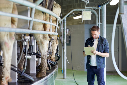 Obraz na plátně man with clipboard and milking cows on dairy farm