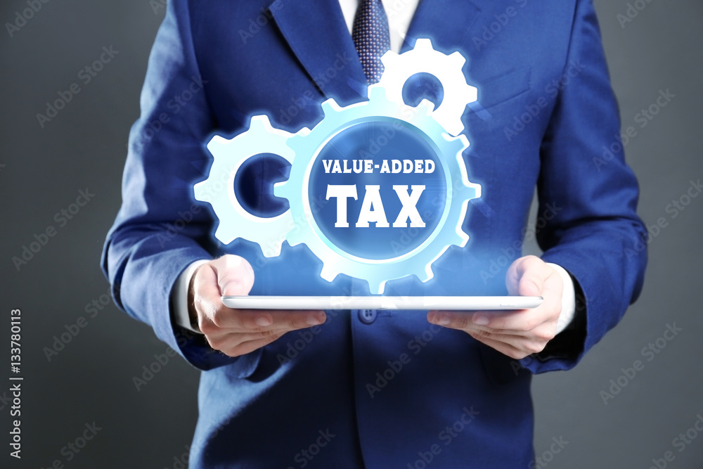 Man holding tablet and gear wheel with text VALUE-ADDED TAX. Taxation concept Man holding tablet and gear wheel with text VALUE-ADDED TAX. Taxation concept