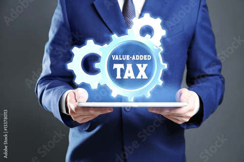 Man holding tablet and gear wheel with text VALUE-ADDED TAX. Taxation concept
