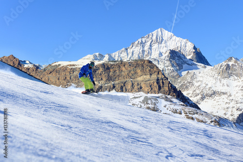 Male snowboarder on the slope with high mountain peaks on background