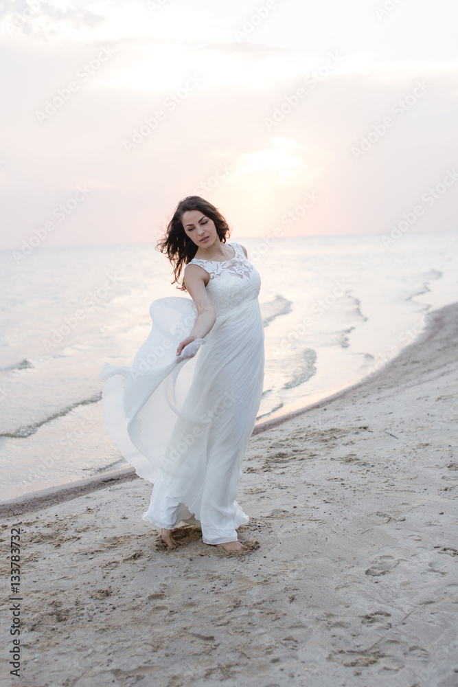 Beautiful young brunette woman in white long dress at the sea shore Beautiful young brunette woman in white long dress at the sea shore