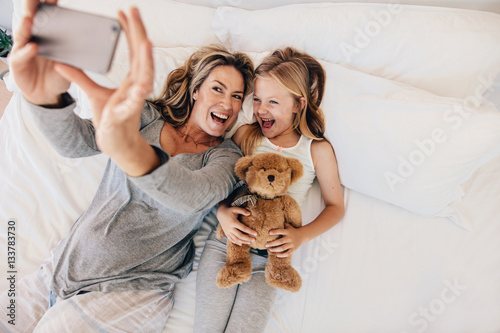 Young mother taking selfie with her daughter on bed