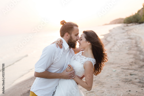 Beach honeymoon couple kissing and hugging on white sand beach. Newlyweds happy in love relaxing on summer holidays. Travel vacation concept.