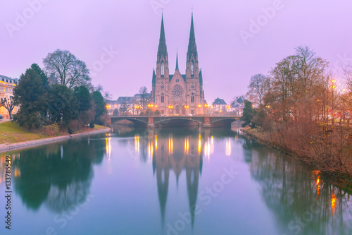 Picturesque foggy Reformed Saint Paul church with mirror reflections in the river Ile during morning blue hour  Strasbourg  Alsace  France