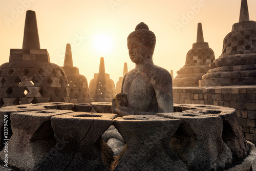 Buddha statue with sunshine through mist and pagodas at Borobudur temple