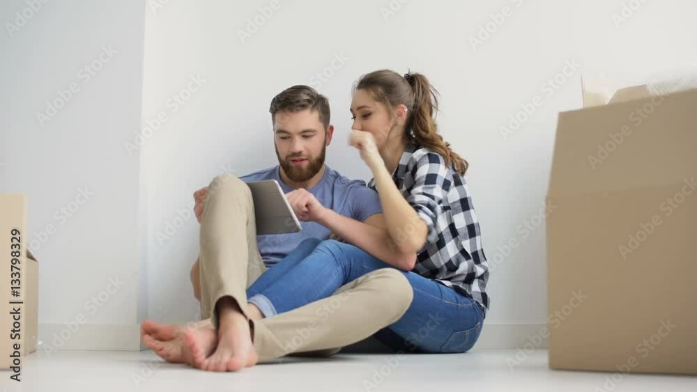 Young happy couple with digital tablet sitting on the floor in their new home