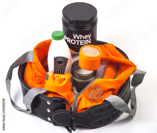 Orange bag with jar and cup with whey chocolate protein, shaker with fat free milk, cap of shaker, bottle with milk. Athletic belt around the bag. Fitness and bodybuilding diet for growing muscles.