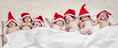 Seven little newborn children wearing Santa Claus