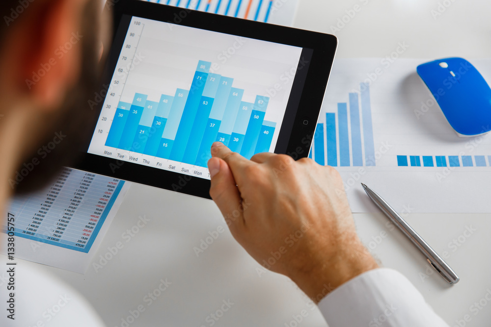 Business person analyzing financial statistics displayed on the tablet screen Business person analyzing financial statistics displayed on the tablet screen