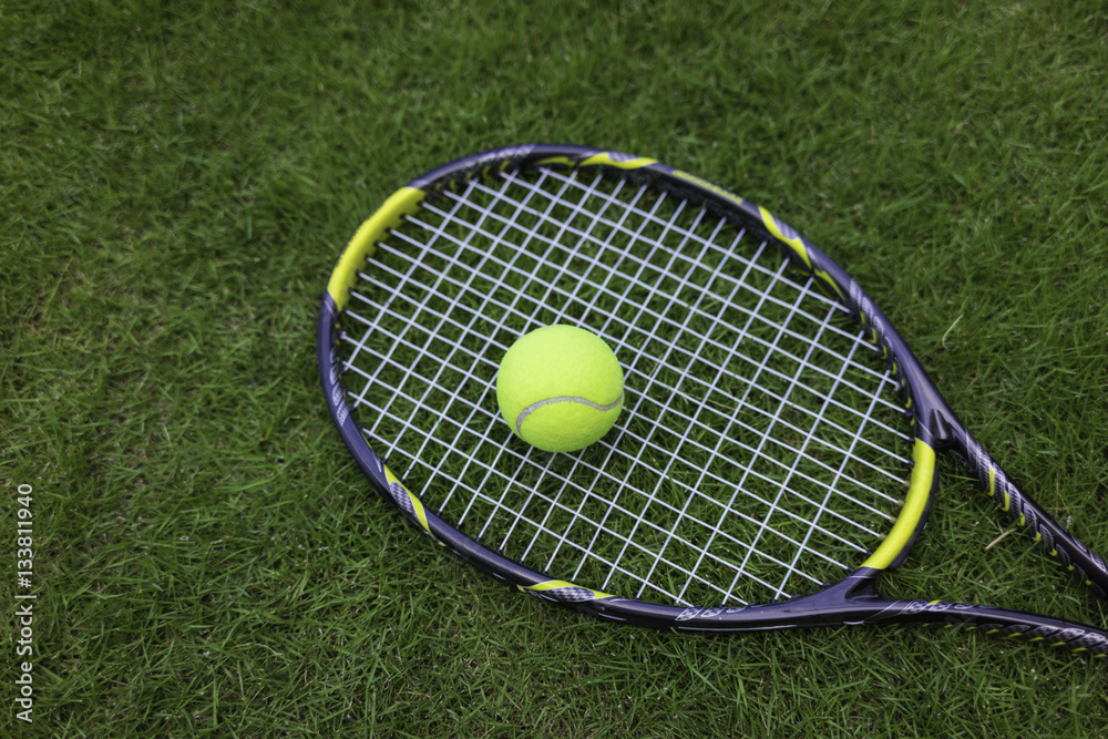 Tennis ball and racket on green grass background