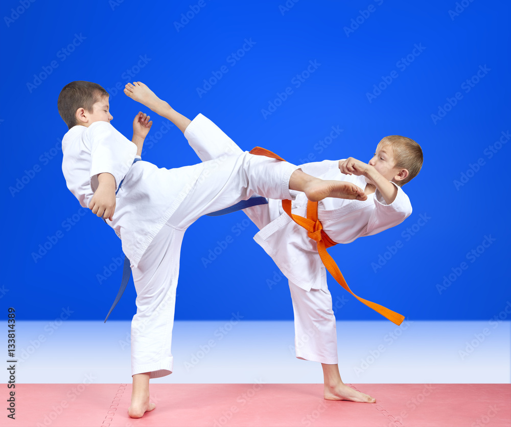 On a blue background two athletes train kick leg On a blue background two athletes train kick leg
