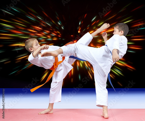 Against the background of bright rays of two athletes are beating kicks