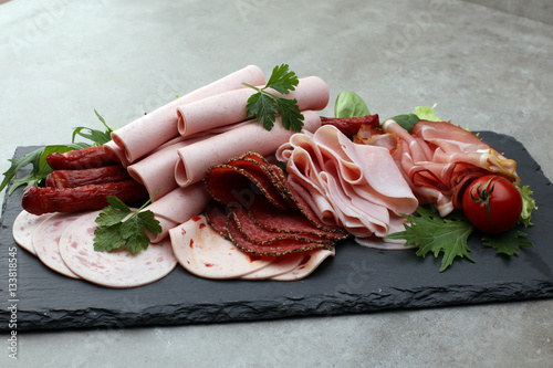 Food tray with delicious salami, pieces of sliced ham, sausage, tomatoes, salad and vegetable - Meat platter with selection
