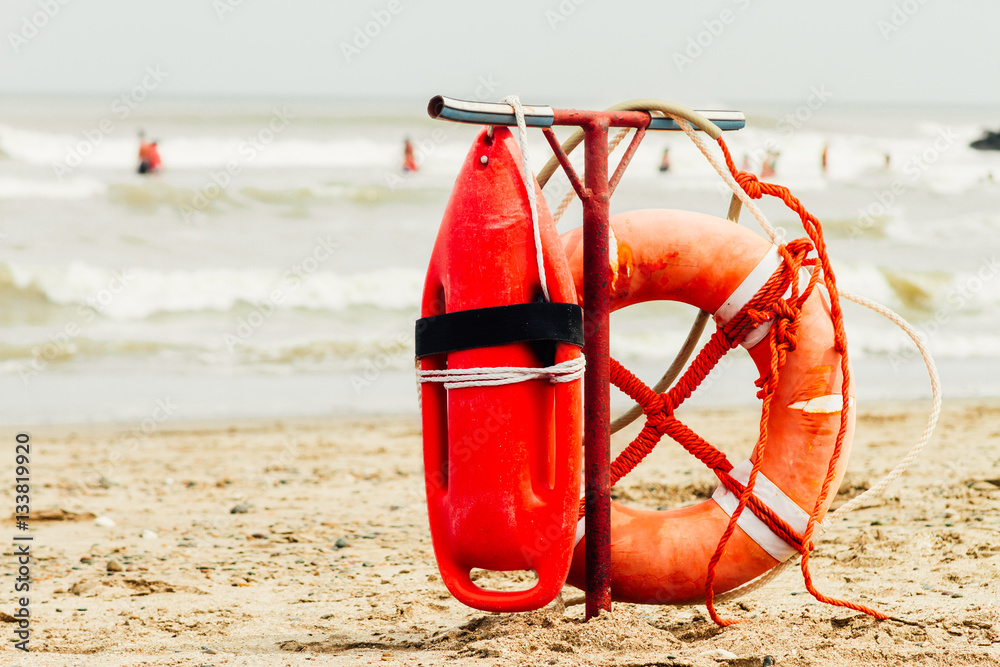 Ring buoy and can of lifeguard on the beach with sea with people - obrazy, fototapety, plakaty 