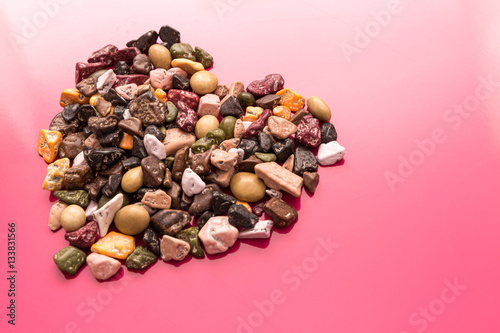 edible chocolate pebbles forming heart on pink mirror surface