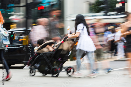 Young mother pushing the pushchair. Lots of people walking in Oxford street, London. Blurred image. 