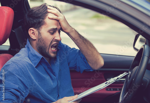 Stressed desperate man driver with papers sitting inside car photo