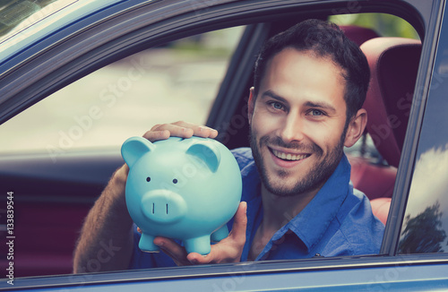 Happy man sitting inside his new car holding piggy bank